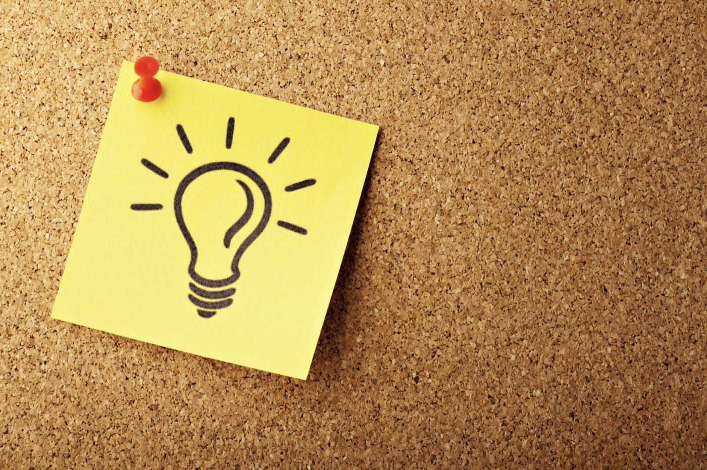 Sticky note with a hand-drawn light bulb pinned to a cork board